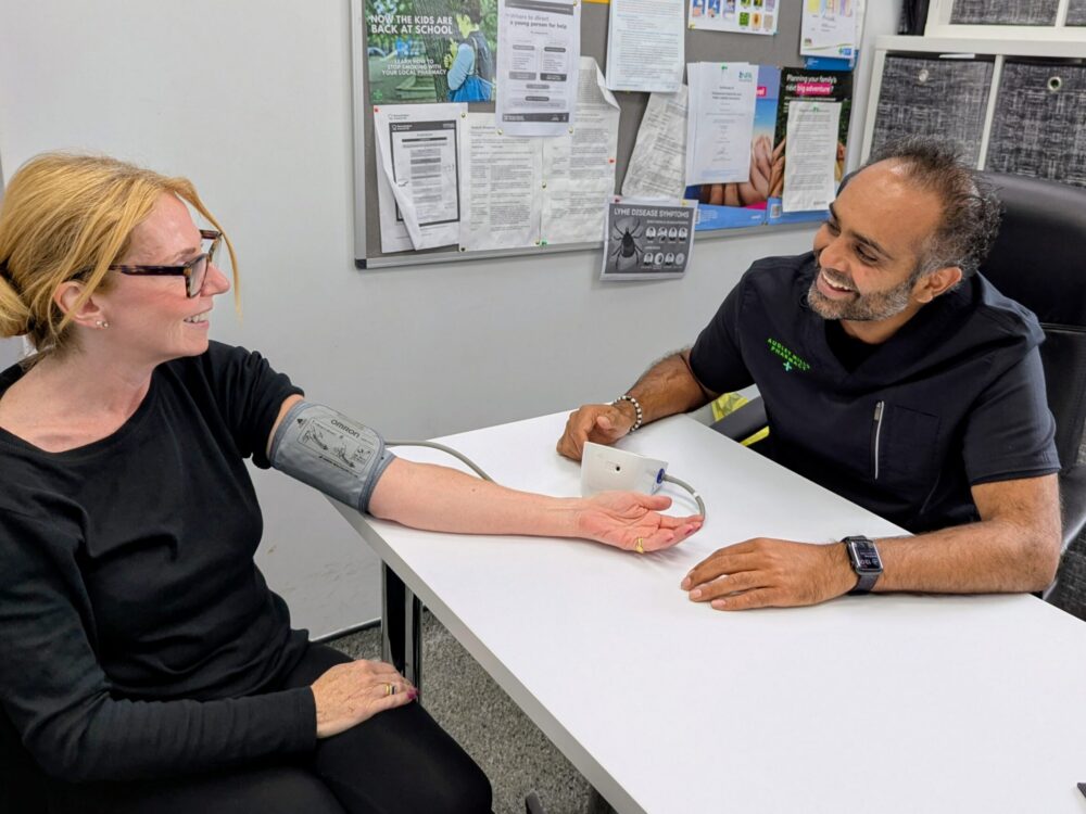 Patient having their blood pressure checked by a healthcare professional using a digital blood pressure monitor in a clinic.